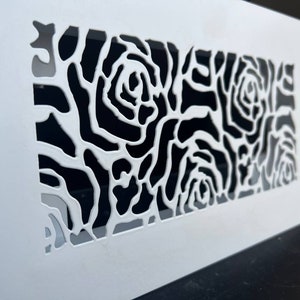 Puede incluir: Rejilla de ventilación de pared blanca con un patrón de rosas en blanco y negro recortado.