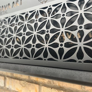 Op de afbeelding: Een zwarte metalen wanddecoratie met een geometrisch patroon van overlappende cirkels en bloemvormen. Het metaal is uitgesneden om een decoratief ontwerp te creëren. De tekst "SAVA ART METAL" is zichtbaar in de linkerbovenhoek.