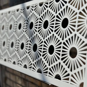 May include: White metal decorative screen with a geometric pattern of repeating circles and radiating lines. The screen is made of thin metal and has a modern design.