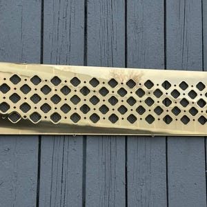 Puede incluir: Una rejilla de ventilación rectangular de latón con una cuadrícula de aberturas en forma de diamante. La cubierta de ventilación tiene una superficie pulida y reflectante y una fina malla visible a través de las aberturas. Diseñada para la circulación del aire.