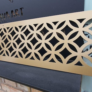 May include: Gold metal vent cover with a geometric pattern of overlapping circles and diamonds. The vent cover is approximately 61 cm long and 20 cm wide.