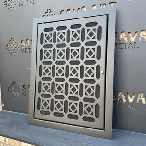 May include: A black metal vent cover with a geometric pattern. The vent cover is mounted on a black wall with the text "Sava Art Metal" printed on it.