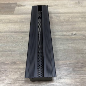 May include: Black metal vent cover with a rectangular shape and a series of horizontal lines. The vent cover has a small opening with a perforated pattern.