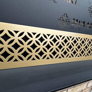 May include: A gold metal vent cover with a geometric pattern of overlapping circles. The vent cover is approximately 20 inches long and 4 inches wide.