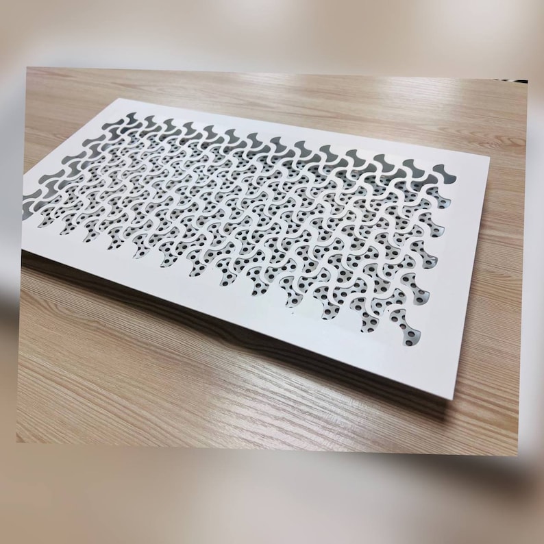 K&ouml;nnte beinhalten: Wei&szlig;er L&uuml;ftungsgitter aus Metall mit einem dekorativen Muster aus &uuml;berlappenden Kreisen und Kurven.
