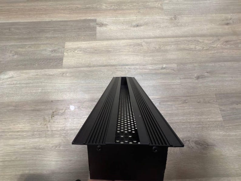 May include: Black metal light fitting with a rectangular shape and a grid pattern. The fitting has a long, narrow design with a series of parallel lines running along the top and bottom.