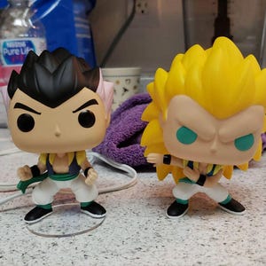 Puede incluir: Dos figuras de estilo anime, una con cabello negro y un atuendo rosa y verde, la otra con cabello amarillo y un atuendo verde y azul.