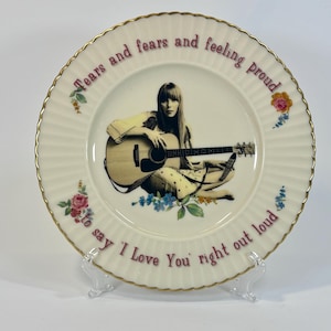 May include: A decorative plate featuring a seated figure with a guitar. The plate has a cream-colored background with a gold rim and floral accents. Text on the plate reads "Tears and fears and feeling proud to say I Love You right out loud."