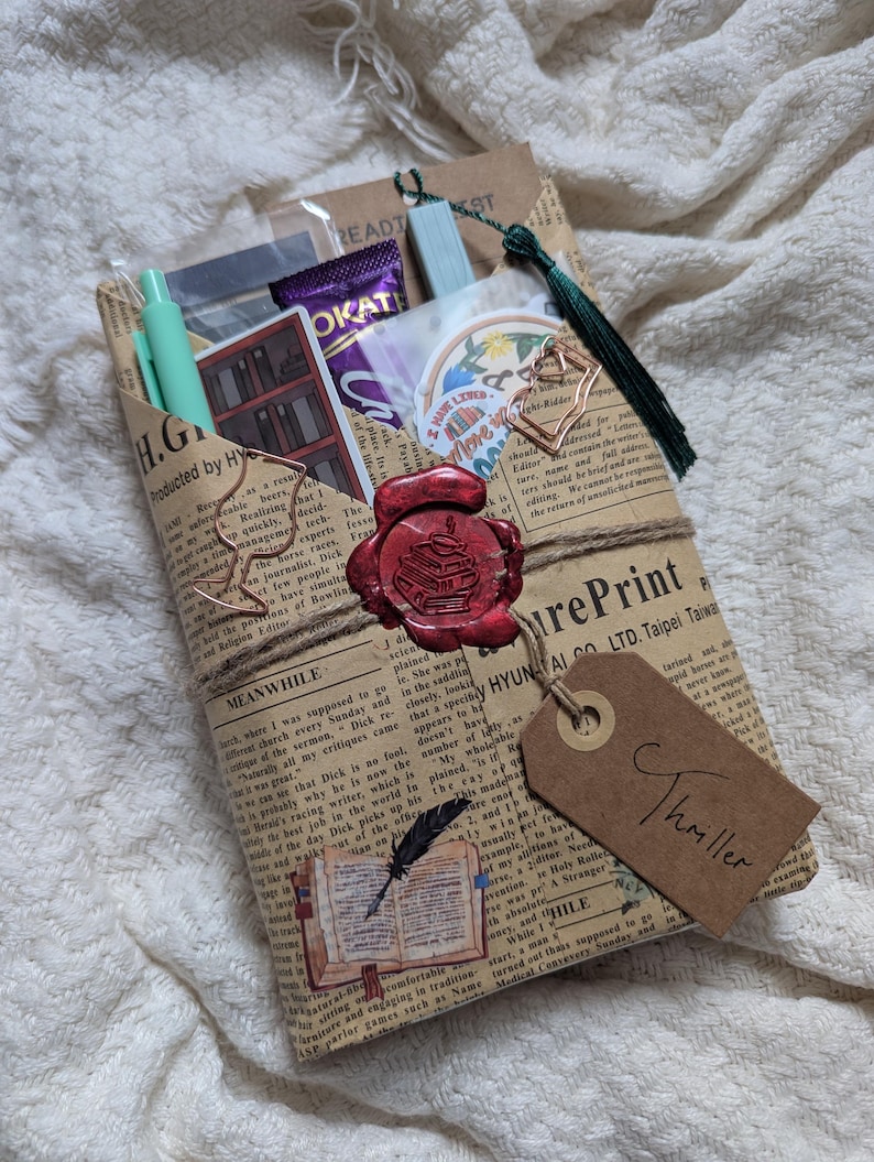 May include: A wrapped gift package with a vintage newspaper print. It's sealed with a red wax stamp and tied with twine. A tag reads "Thriller." Inside are pens, stickers, and a chocolate bar. A green tassel hangs from the top.