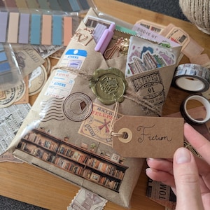 May include: A wrapped package with a brown paper exterior, adorned with vintage-style stamps and a wax seal. A brown tag with the word "Fiction" is attached. The package is surrounded by stationery supplies, including washi tape and sticky notes.