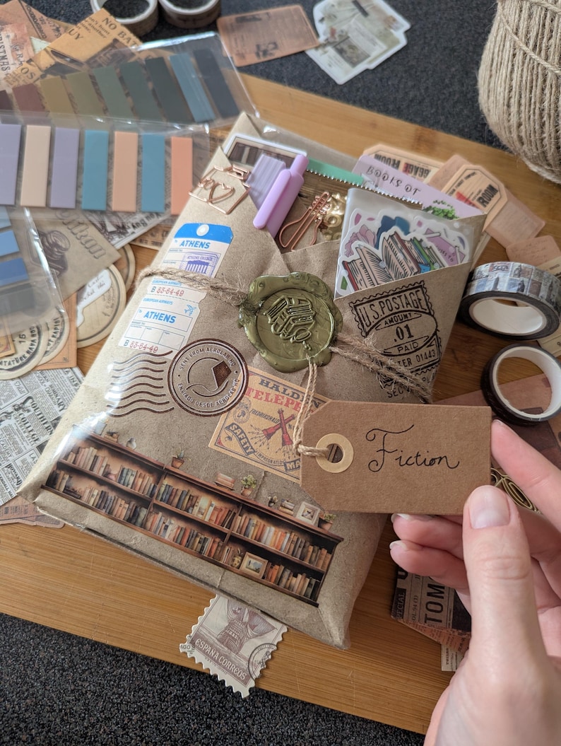 May include: A wrapped package with a brown paper exterior, adorned with vintage-style stamps and a wax seal. A brown tag with the word "Fiction" is attached. The package is surrounded by stationery supplies, including washi tape and sticky notes.