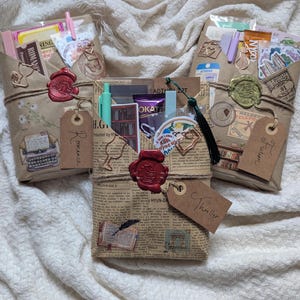 May include: Three gift packages wrapped in brown paper, tied with twine, and sealed with wax stamps. Each package contains various items, including stickers, pens, and tags labeled "Romance", "Fiction", and "Thriller". The packages are decorated with vintage-style illustrations and text.