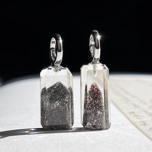 May include: Two rectangular pendants with silver loops. The clear, faceted pendants contain dark grey and reddish-brown mineral inclusions. The pendants are displayed against a dark background.