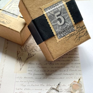 May include: Three clear glass pendants with gold accents and different colored crystals inside. The crystals are pink, gold, and red. The pendants are sitting on a piece of paper with handwritten text.