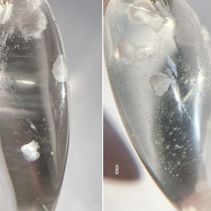 May include: Close-up of two clear quartz crystals with white inclusions. The crystals are oval shaped and have a smooth, polished surface.