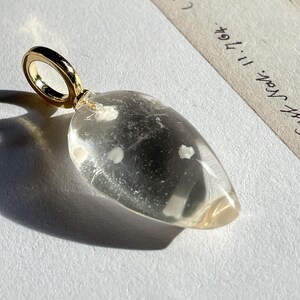 May include: A clear glass pendant with a gold loop. The glass has small white inclusions throughout.