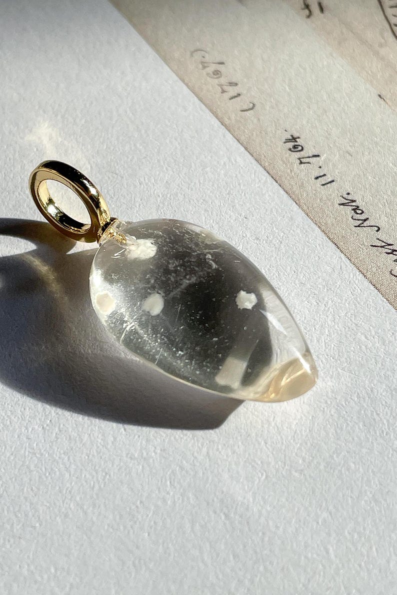 May include: A clear glass pendant with a gold loop. The glass has small white inclusions throughout.