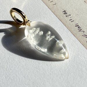 May include: A clear teardrop-shaped pendant with a gold bail. The pendant contains small white inclusions.