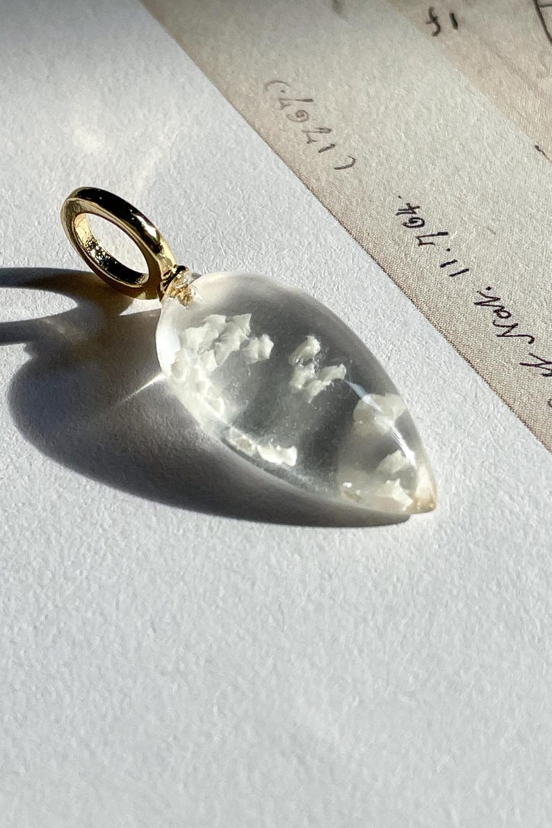 May include: A clear teardrop-shaped pendant with a gold bail. The pendant contains small white inclusions.