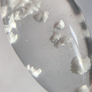 May include: A clear teardrop-shaped pendant with a gold bail. The pendant contains small white inclusions.