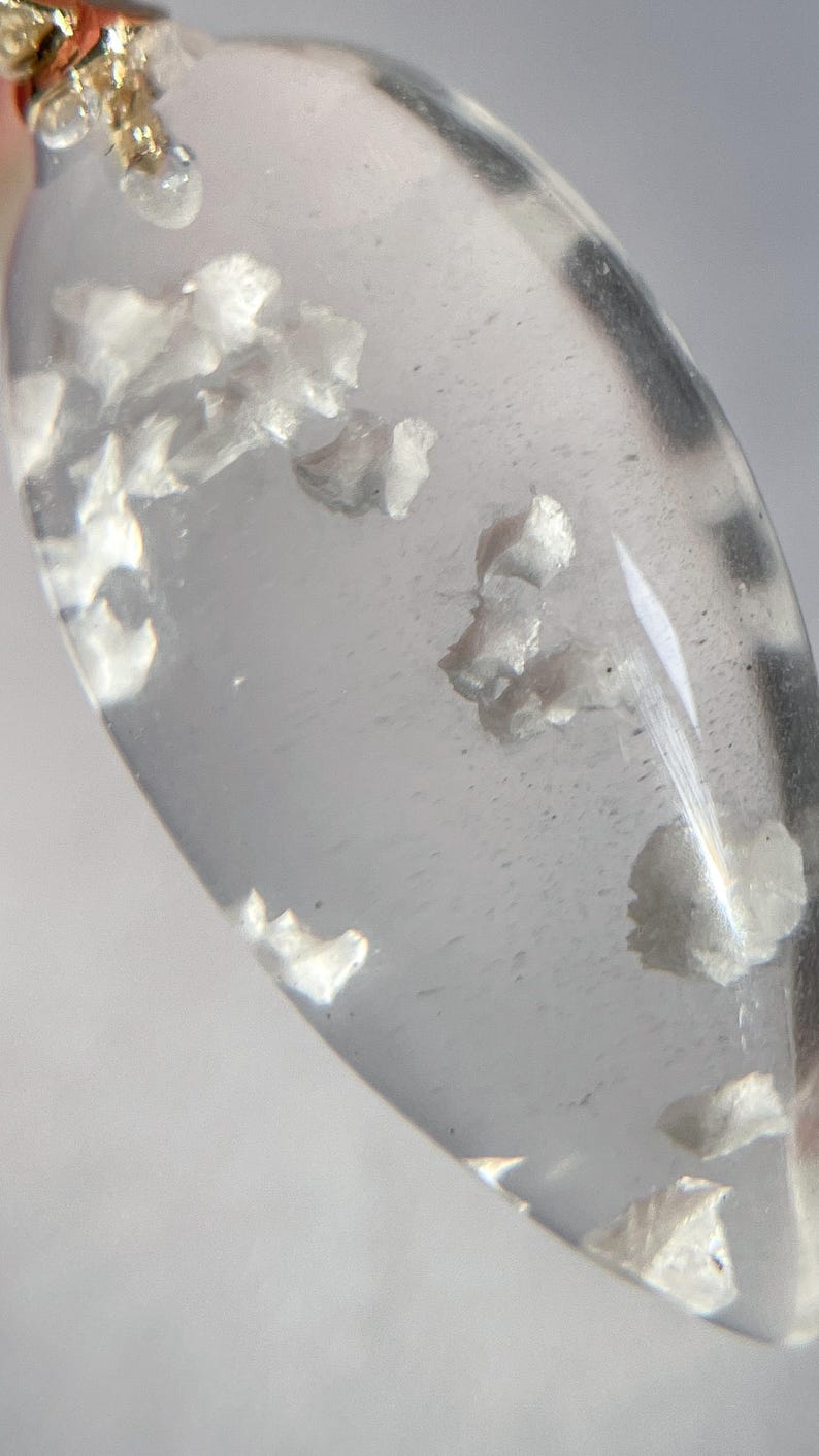 May include: A clear teardrop-shaped pendant with a gold bail. The pendant contains small white inclusions.