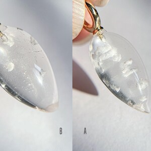 May include: A clear teardrop-shaped pendant with a gold bail. The pendant has a cloudy, milky appearance with white inclusions.