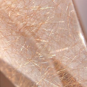 May include: Close-up of a clear quartz crystal with golden rutile inclusions. The crystal is translucent, with numerous needle-like rutile strands creating a striking, textured pattern. The light catches the golden strands, creating a shimmering effect.