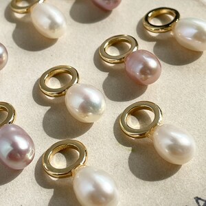 Puede incluir: Una colección de dijes de oro con detalles de perlas. Algunas perlas son blancas y otras son rosadas.