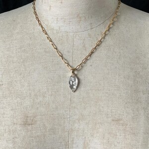 May include: A gold chain necklace with a clear crystal pendant shaped like a teardrop.