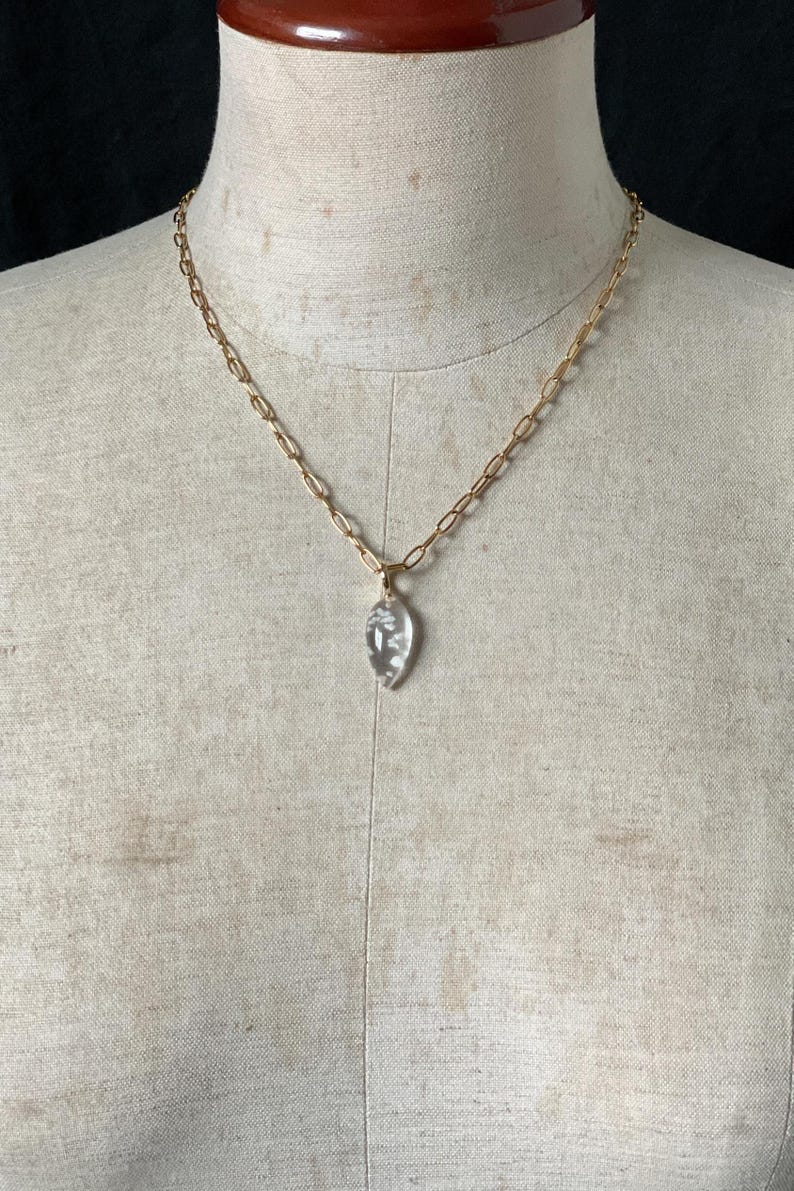 May include: A gold chain necklace with a clear crystal pendant shaped like a teardrop.