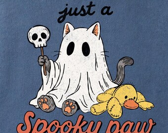 May include: A blue t-shirt featuring a graphic of a cat dressed as a ghost, holding a skull on a stick, with a yellow plush duck toy. The text reads just a Spooky paw in black and orange lettering. The shirt has a crew neckline and short sleeves.