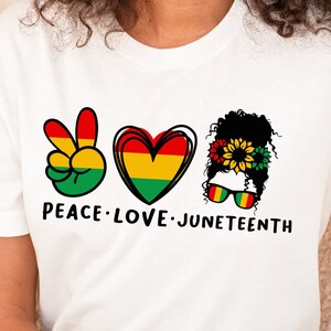 May include: White t-shirt with a peace sign, heart, and a woman with a sunflower crown. The text "Peace Love Juneteenth" is printed on the shirt.