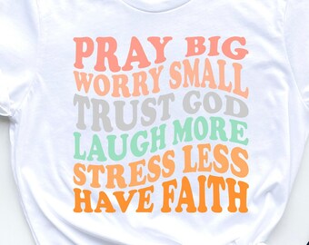 May include: White t-shirt with a colorful graphic that reads "Pray Big Worry Small Trust God Laugh More Stress Less Have Faith".