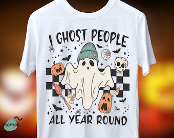 May include: White t-shirt with a ghost wearing a beanie and the text "I ghost people all year round". The design also includes pumpkins, bats, candy corn, and a skull.