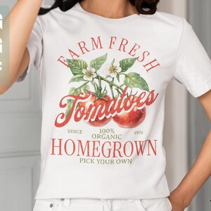 May include: White t-shirt with a red, green, and white graphic design that says "Farm Fresh Tomatoes" with a vine of tomatoes and leaves. The text also says "Since 1976, 100% Organic, Homegrown, Pick Your Own."