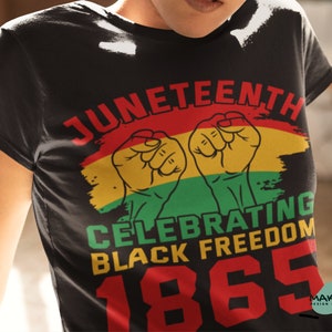 Puede incluir: Camiseta negra con un diseño gráfico que celebra el Juneteenth. El diseño presenta un esquema de color rojo, amarillo y verde con puños levantados y el texto "Juneteenth Celebrating Black Freedom 1865".