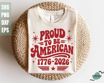 May include: Cream-colored t-shirt with the text "PROUD TO BE AMERICAN 1776-2026" in red, retro-style lettering. The design includes stars and stripes, evoking a patriotic theme. The shirt is displayed on a woven, circular surface.