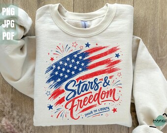 May include: Cream-colored sweatshirt featuring a distressed American flag design in red and blue, with the words "Stars & Freedom" in a script font. The phrase "Shine in Liberty" is below the main text. The sweatshirt is folded.