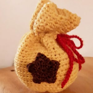 Könnte beinhalten: Eine gehäkelte gelbe Tasche mit einem braunen Stern und einem roten Band.