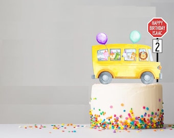 Puede incluir: Una tarta de cumpleaños con chispas de colores, coronada con un adorno de tarta de autobús escolar amarillo. El autobús tiene pasajeros animales, globos y letreros que dicen "Happy Birthday Isaac" y "I am 2".