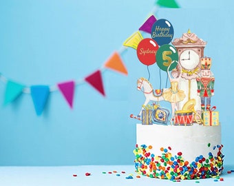 May include: A white cake decorated with colorful sprinkles and a whimsical cake topper featuring a ballerina, a rocking horse, a nutcracker, a clock, and balloons that say "Happy Birthday" and "Sydney".