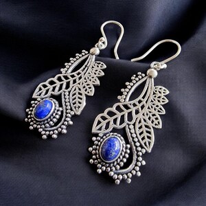 Könnte beinhalten: Silberne Ohrringe mit einem blauen Edelstein und einem Blattdesign.