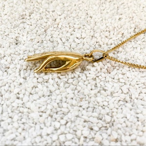 Può includere: Una collana d'oro con un ciondolo a forma di mano. La mano è in un gesto di pace o benedizione.