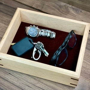 May include: A wooden tray with a burgundy felt lining. The tray contains a silver watch, a set of keys with a key chain, and a pair of black eyeglasses.