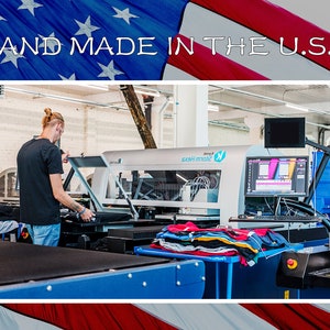 Peut inclure: Une personne utilisant une grande machine d'impression industrielle dans un environnement d'usine. La machine est utilis&eacute;e pour imprimer des motifs sur du tissu. Le texte "HAND MADE IN THE U.S.A." est affich&eacute; au-dessus de l'image.