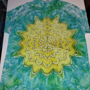 May include: A tie-dye t-shirt with a large yellow mandala design in the center. The background is a mix of blue, green, and white.
