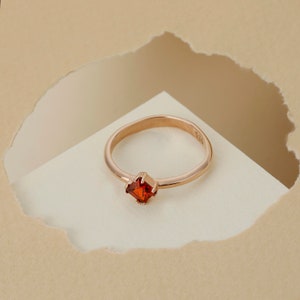 May include: A rose gold ring with a square red gemstone.