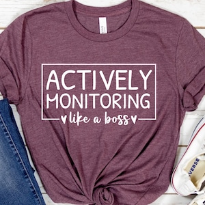 May include: A maroon t-shirt with the text "ACTIVELY MONITORING - like a boss -" in white.
