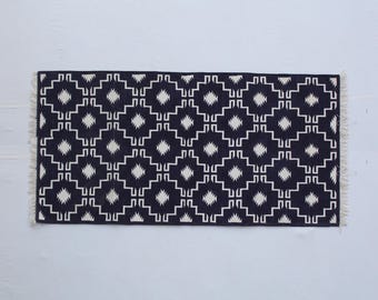 Könnte beinhalten: Schwarz-weißer geometrischer Teppich mit Fransenrand. Der Teppich hat ein sich wiederholendes Muster aus Quadraten und Rauten.