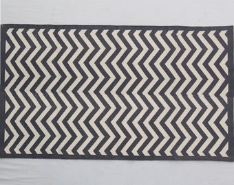 Könnte beinhalten: Schwarz-weißer Teppich mit Chevron-Muster. Der Teppich hat ein schlichtes Design mit abwechselnden schwarzen und weißen Streifen, die ein Chevron-Muster bilden.